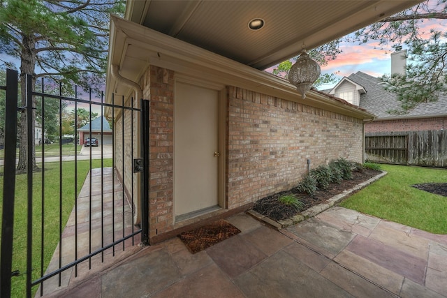 exterior entry at dusk with fence, a lawn, and brick siding