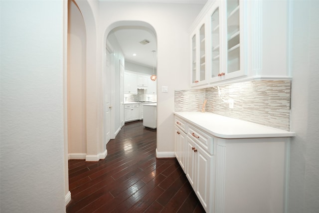 bar featuring arched walkways, dark wood-style flooring, visible vents, baseboards, and decorative backsplash