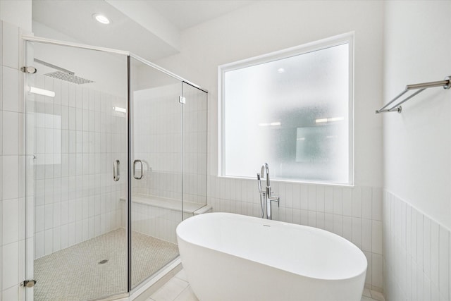 full bath with a stall shower, a freestanding tub, tile patterned flooring, and tile walls