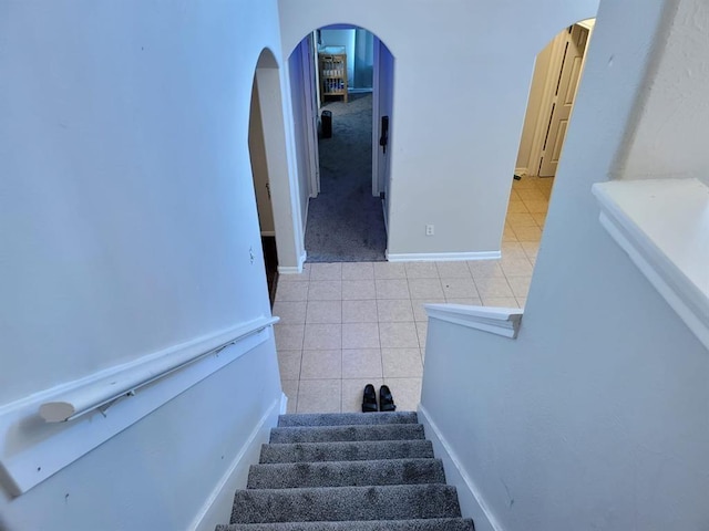 staircase with arched walkways, baseboards, and tile patterned floors