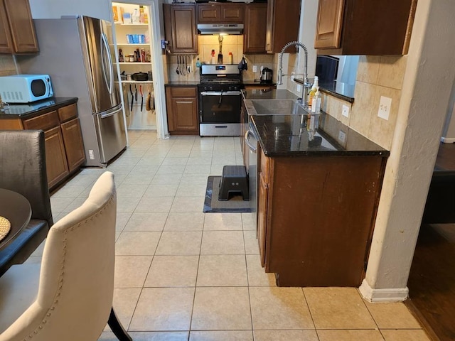 kitchen featuring light tile patterned floors, decorative backsplash, a sink, under cabinet range hood, and stainless steel gas range oven