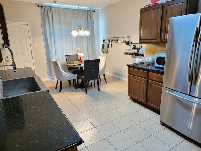 kitchen featuring light tile patterned floors, tasteful backsplash, dark countertops, freestanding refrigerator, and a chandelier