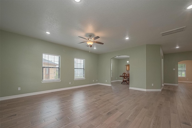 spare room featuring baseboards, visible vents, arched walkways, a ceiling fan, and light wood-style flooring