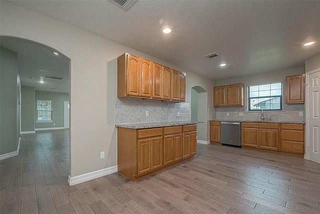 kitchen with visible vents, arched walkways, a healthy amount of sunlight, light wood-style floors, and stainless steel dishwasher