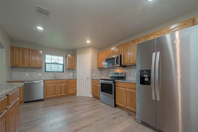 kitchen with stainless steel appliances, a sink, visible vents, light wood-type flooring, and tasteful backsplash