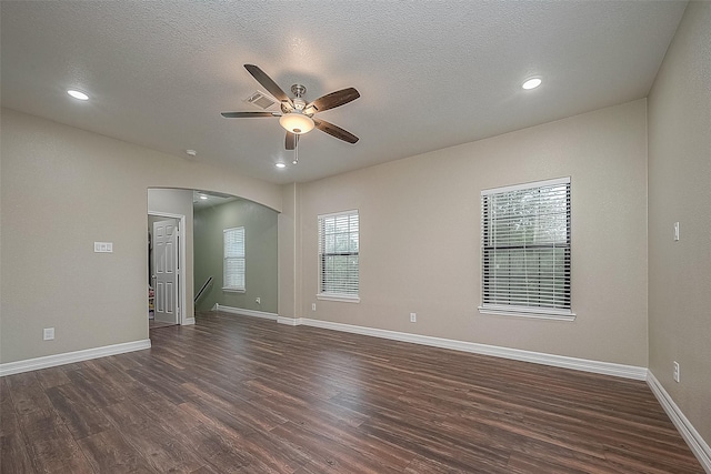 unfurnished room featuring arched walkways, dark wood-style flooring, a textured ceiling, and baseboards