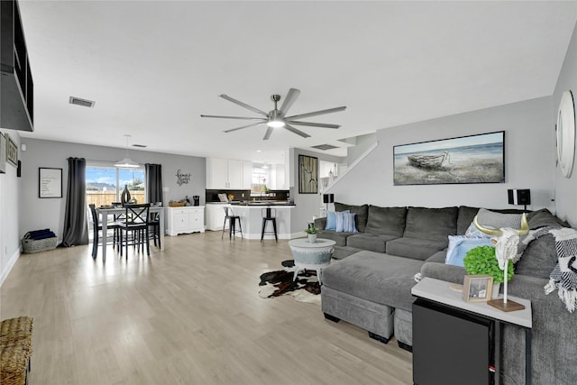 living area featuring light wood finished floors, baseboards, visible vents, and a ceiling fan