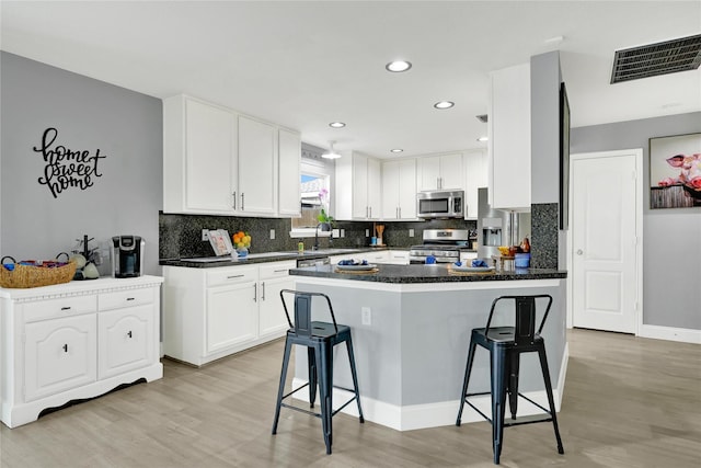 kitchen with white cabinets, dark countertops, a kitchen bar, and stainless steel appliances