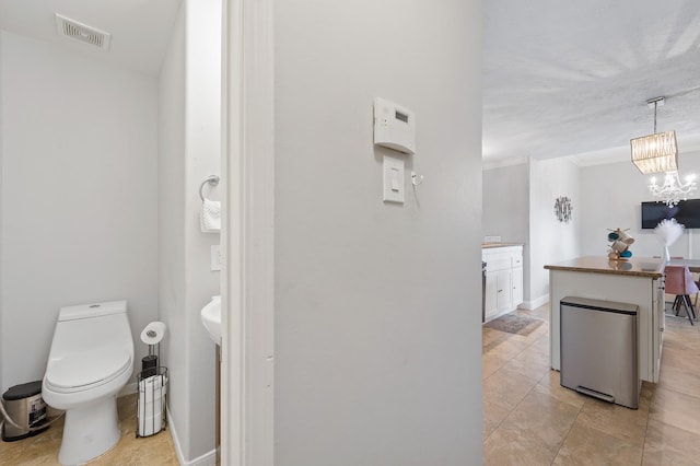 half bathroom featuring visible vents, toilet, an inviting chandelier, ornamental molding, and baseboards