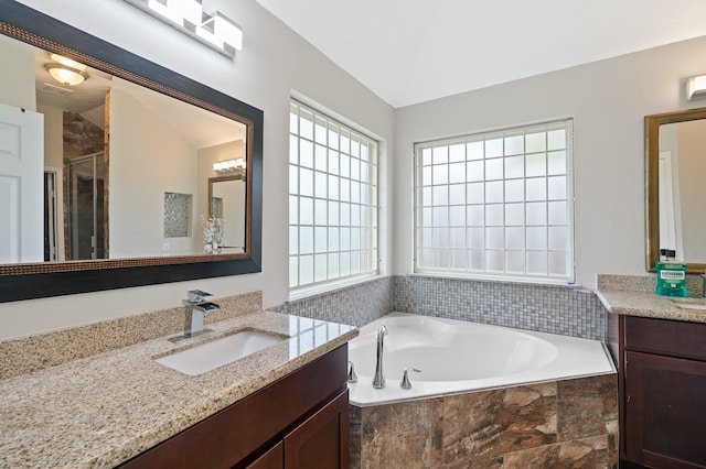 bathroom featuring lofted ceiling, a garden tub, two vanities, and a sink