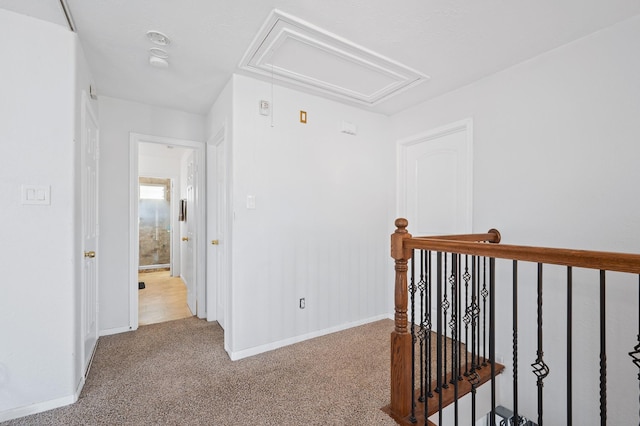 corridor with an upstairs landing, attic access, baseboards, and light colored carpet