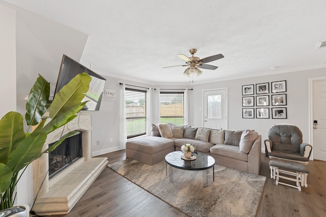 living room with visible vents, dark wood finished floors, a ceiling fan, crown molding, and a fireplace