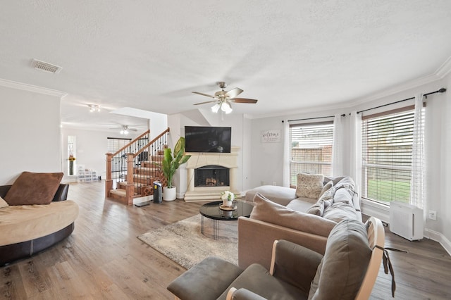 living room featuring a fireplace with raised hearth, a textured ceiling, wood finished floors, visible vents, and stairway