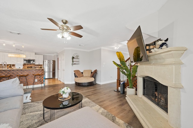 living room with a fireplace, visible vents, light wood-style floors, ornamental molding, and baseboards