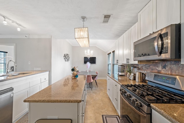 kitchen with stainless steel appliances, a sink, white cabinets, hanging light fixtures, and a center island