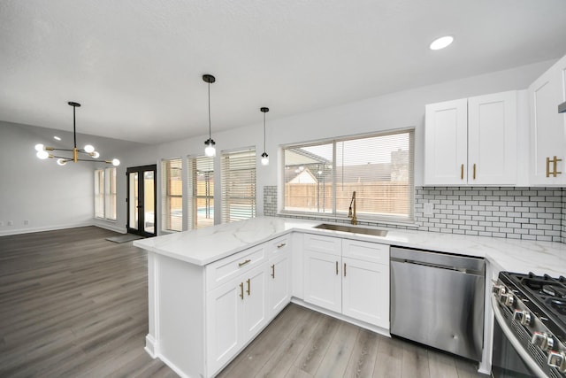 kitchen featuring stainless steel appliances, hanging light fixtures, white cabinets, a sink, and a peninsula