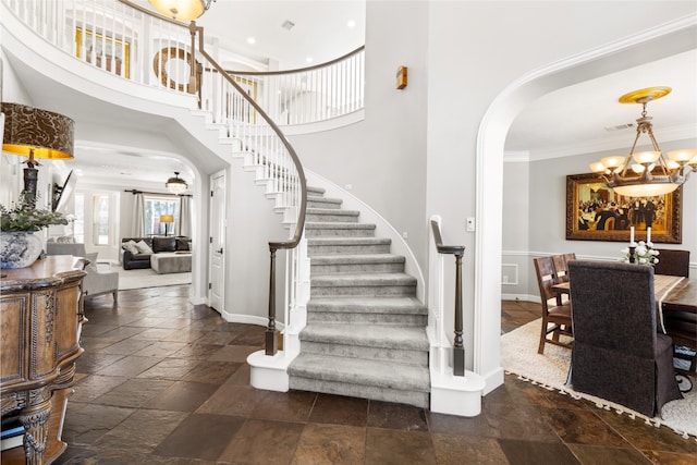 stairway featuring visible vents, arched walkways, an inviting chandelier, crown molding, and stone tile flooring