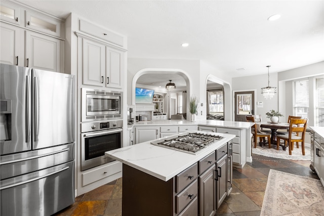 kitchen featuring stainless steel appliances, a peninsula, stone tile flooring, and a center island