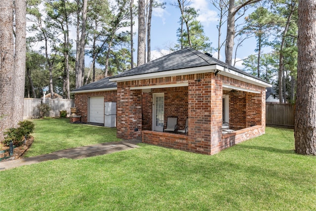 rear view of house with an attached garage, brick siding, fence, roof with shingles, and a lawn