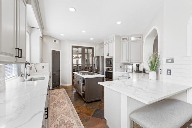 kitchen with light stone counters, stainless steel appliances, a sink, backsplash, and a center island