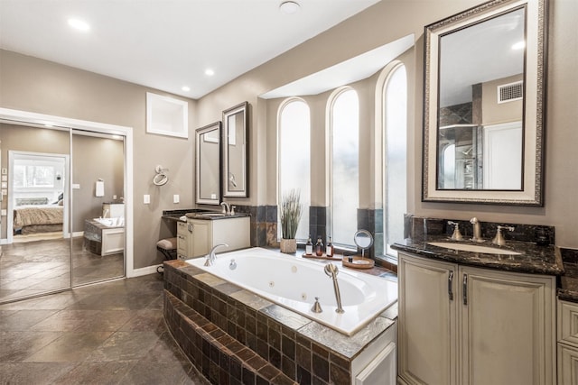 bathroom featuring plenty of natural light, visible vents, a tub with jets, and a sink