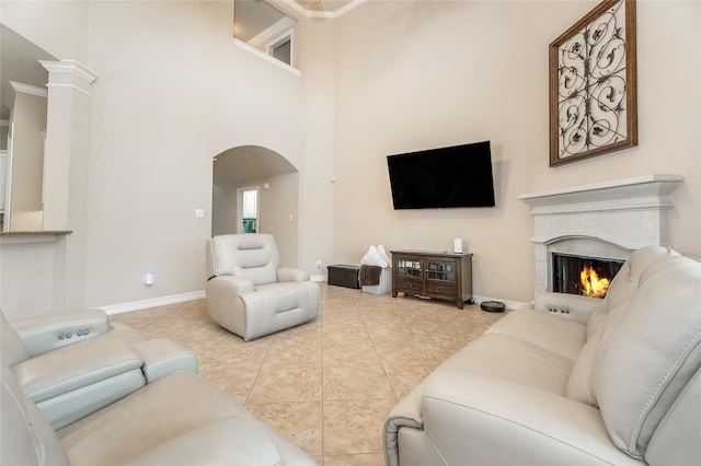 living room with arched walkways, a towering ceiling, tile patterned flooring, a warm lit fireplace, and baseboards