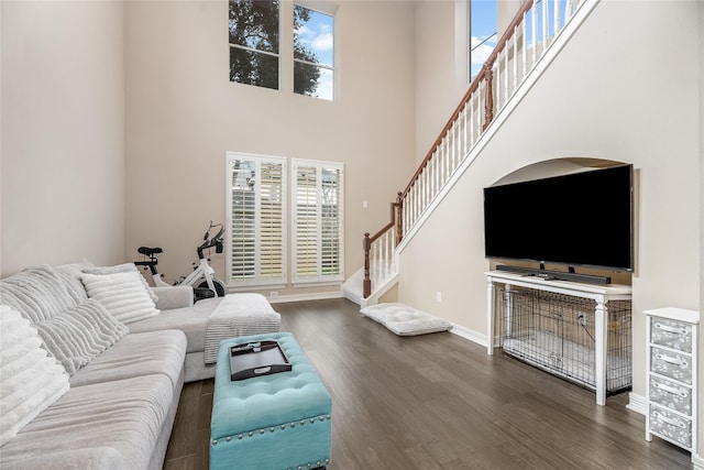 living room featuring dark wood-type flooring, a high ceiling, baseboards, and stairs