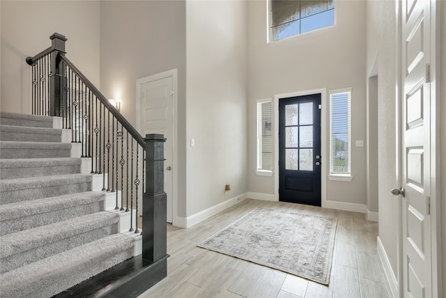 entrance foyer with light wood-type flooring, a high ceiling, baseboards, and stairs