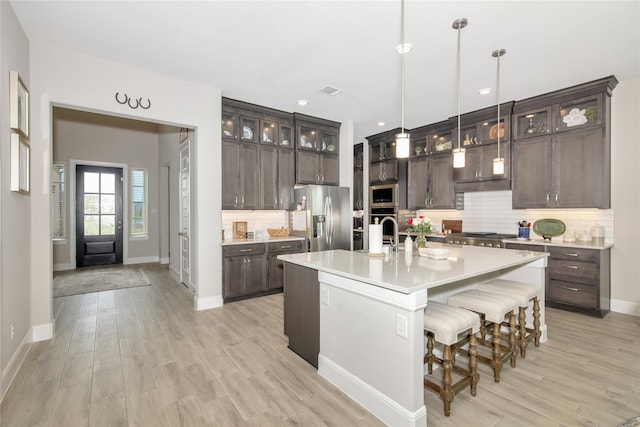 kitchen featuring an island with sink, appliances with stainless steel finishes, light countertops, dark brown cabinets, and pendant lighting