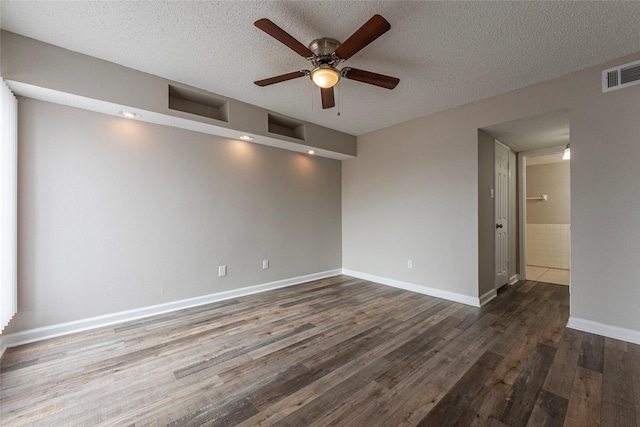 unfurnished room with baseboards, visible vents, a ceiling fan, dark wood-style flooring, and a textured ceiling