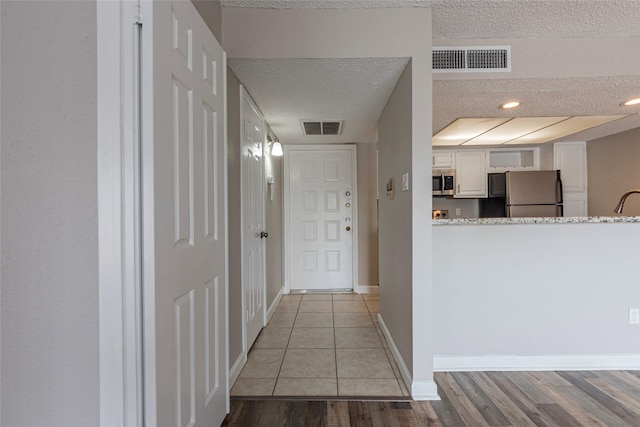 hall with light wood-type flooring, baseboards, visible vents, and a textured ceiling