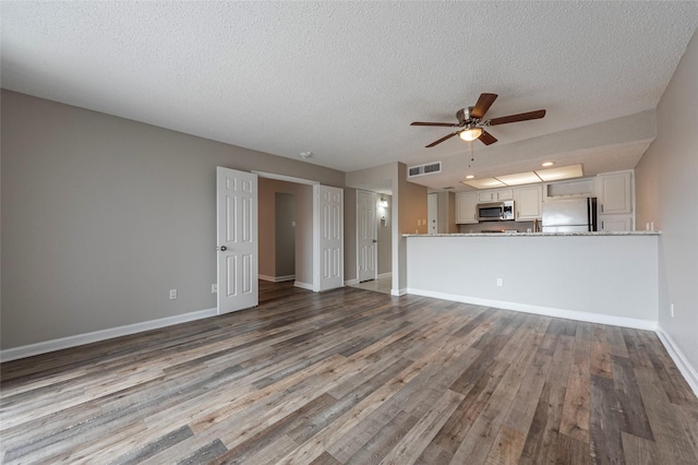 unfurnished living room featuring a textured ceiling, wood finished floors, a ceiling fan, visible vents, and baseboards