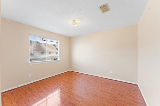 spare room with visible vents, a textured ceiling, baseboards, and wood finished floors