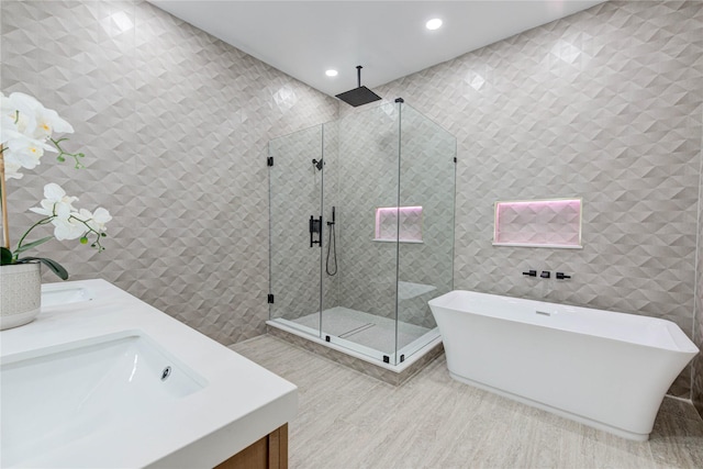 bathroom featuring recessed lighting, tile walls, a freestanding bath, a shower stall, and double vanity