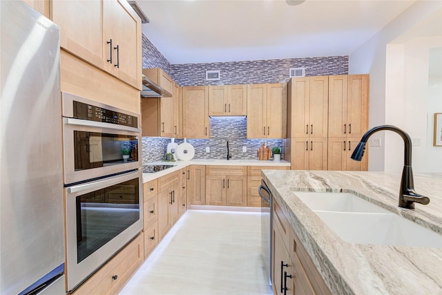 kitchen with appliances with stainless steel finishes, a sink, light stone counters, and light brown cabinetry