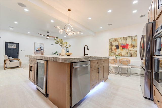 kitchen with decorative light fixtures, visible vents, appliances with stainless steel finishes, a kitchen island with sink, and beverage cooler