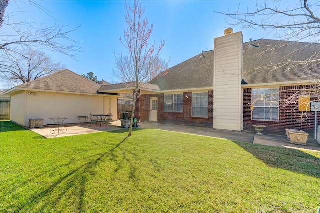 rear view of house with brick siding, roof with shingles, a chimney, a yard, and a patio area