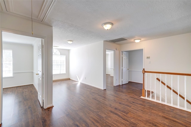 empty room with visible vents, dark wood-type flooring, baseboards, attic access, and a textured ceiling