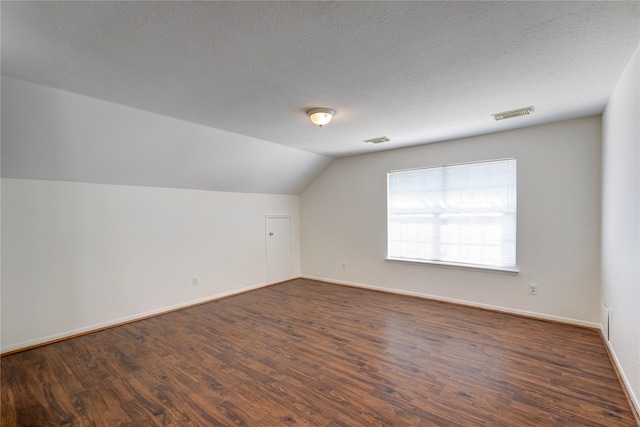 additional living space featuring dark wood finished floors, vaulted ceiling, visible vents, and a textured ceiling