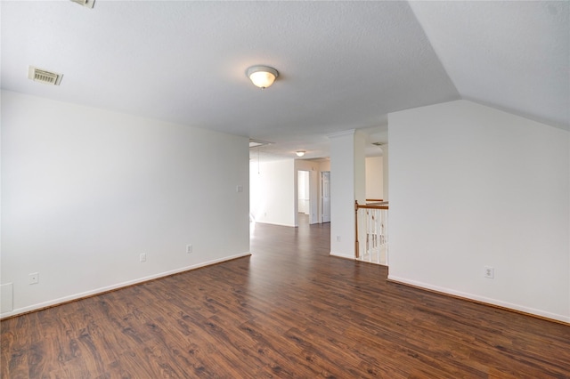 unfurnished room featuring baseboards, visible vents, dark wood finished floors, attic access, and vaulted ceiling