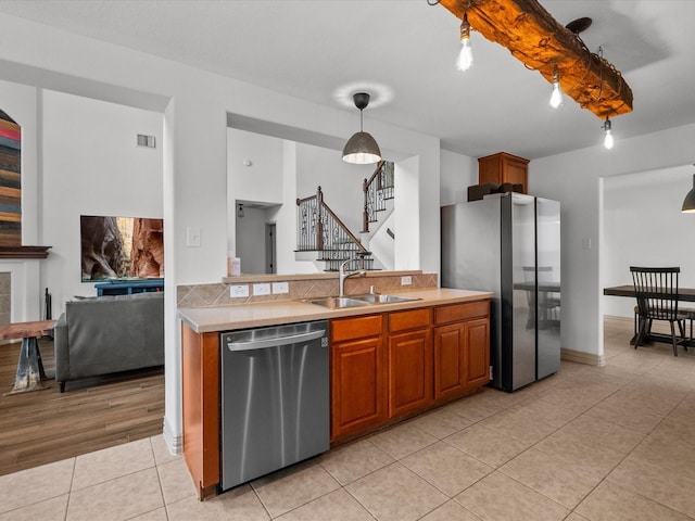 kitchen featuring brown cabinets, stainless steel appliances, light countertops, hanging light fixtures, and a sink