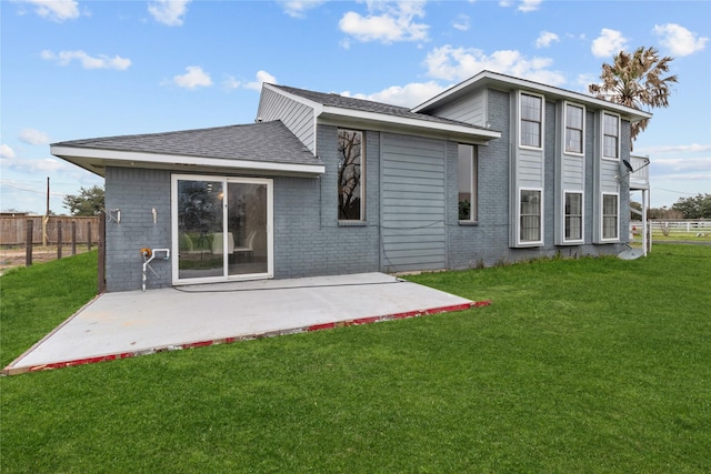 back of property featuring brick siding, fence, a yard, roof with shingles, and a patio area