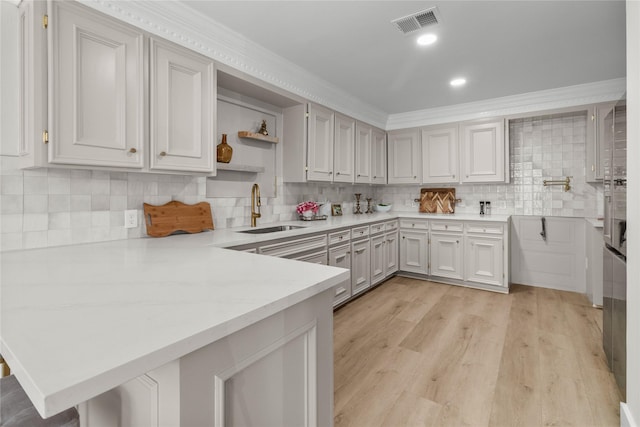 kitchen with open shelves, visible vents, light wood-style floors, a sink, and a peninsula