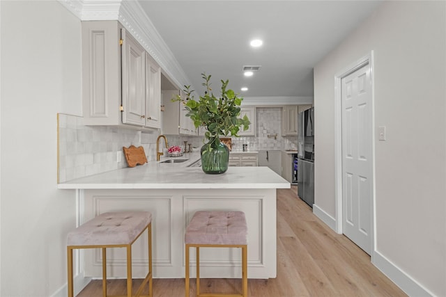 kitchen featuring a breakfast bar area, visible vents, light countertops, a sink, and a peninsula