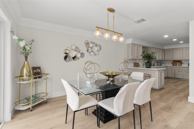 dining room featuring ornamental molding, light wood-style flooring, visible vents, and baseboards