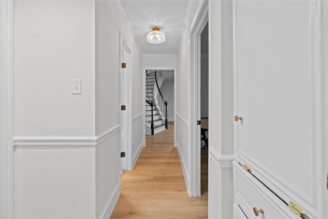 hall with light wood-style floors, stairs, baseboards, and crown molding