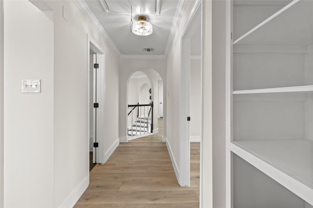 corridor with arched walkways, visible vents, baseboards, ornamental molding, and light wood-type flooring