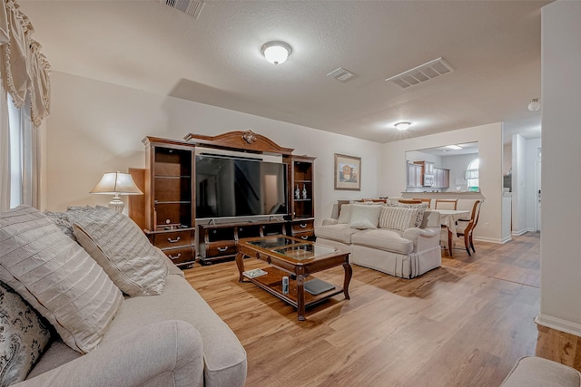 living area featuring baseboards, a textured ceiling, visible vents, and wood finished floors