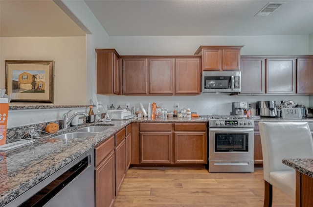 kitchen featuring stainless steel appliances, a sink, visible vents, light wood-type flooring, and light stone countertops