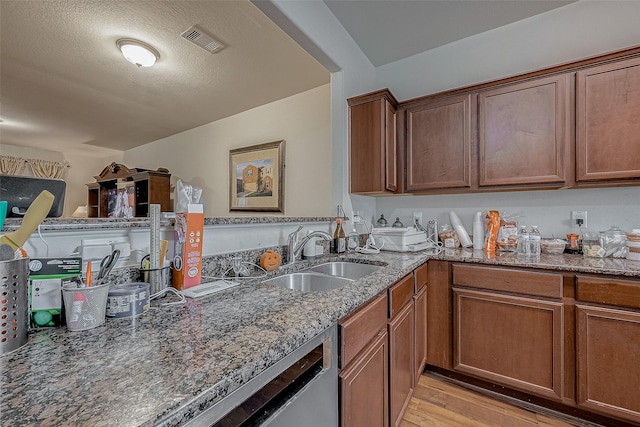 kitchen with a sink, visible vents, light wood-style floors, brown cabinetry, and dark stone countertops